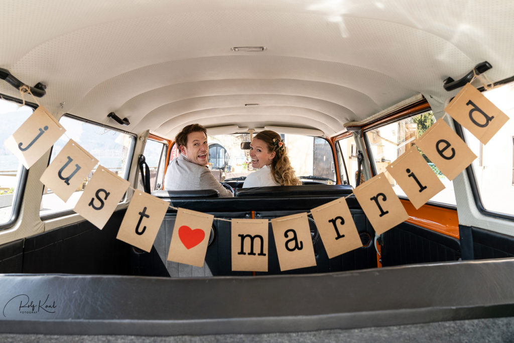 die Buchstaben just-married hängen im Fond eines VW-Bulli - am Steuer sitzt das Brautpaar